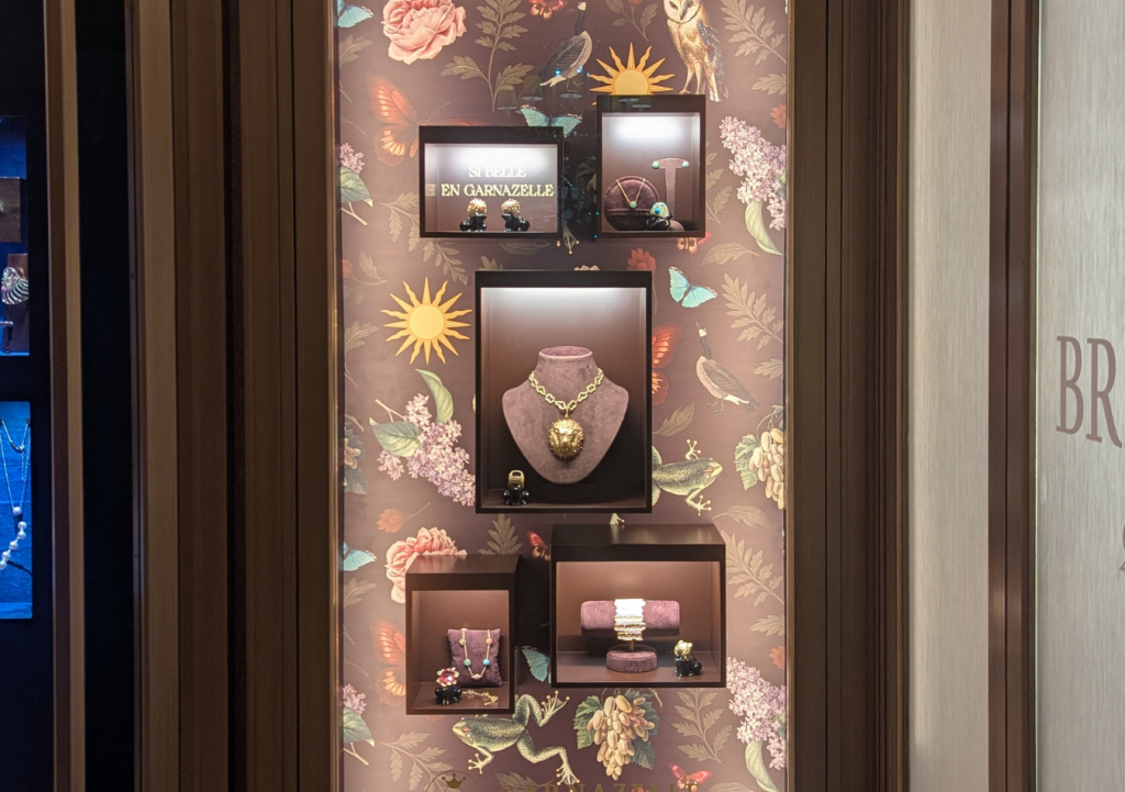 Photographie d'une vitrine de joaillerie, avec un fond de papier peint sur mesure réalisé avec des dessins, et des boîtes éclairées où sont présentés les bijoux.
