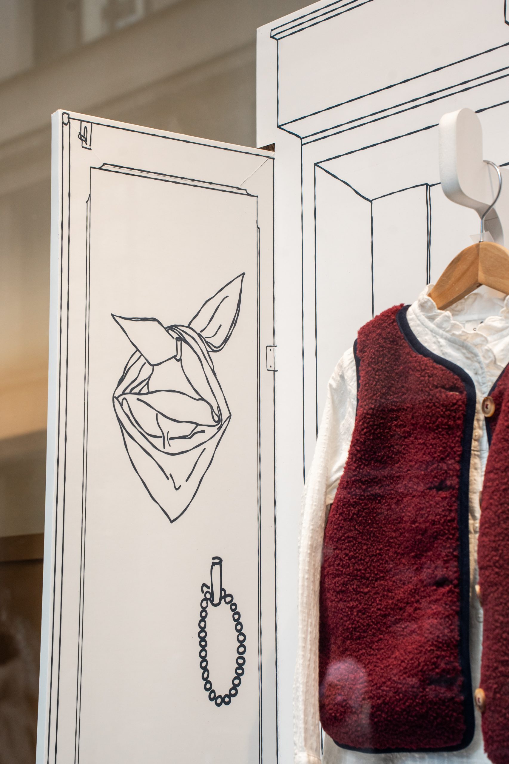 Illustrations sur-mesure d’une vitrine de rentrée : foulard, collier et chaussures dessinés sur les portes d’armoire