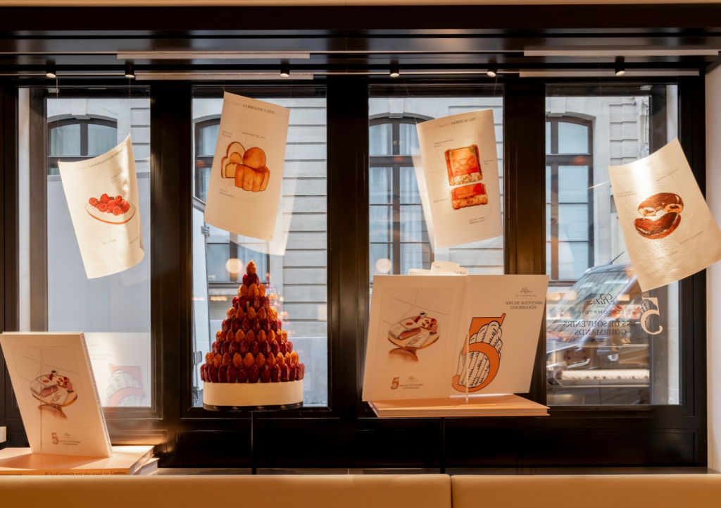 Vitrine anniversaire d’une pâtisserie de luxe à Paris avec un grand livre de conte aux pages suspendues en plein mouvement